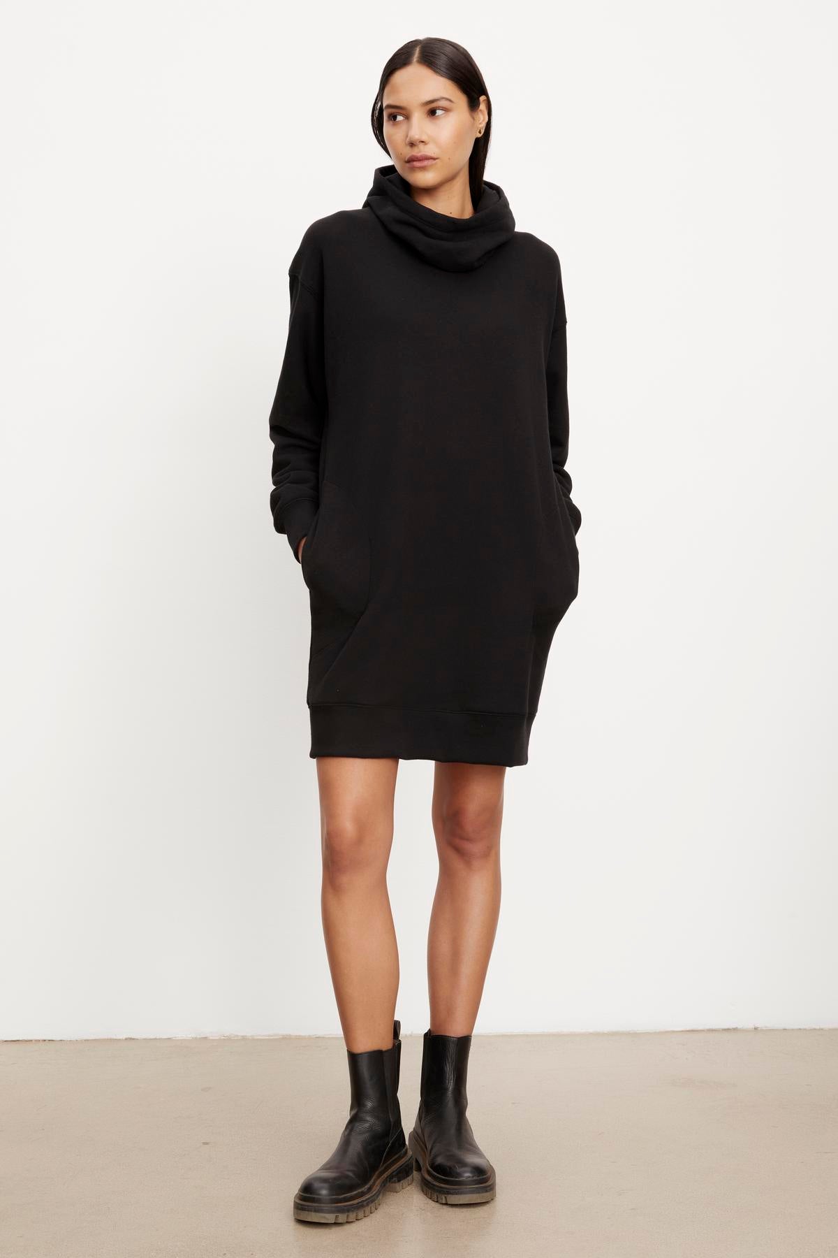 A woman in a YARA SOFT FLEECE HOODIE DRESS by Velvet by Graham & Spencer and black boots standing against a plain background.-35696174366913