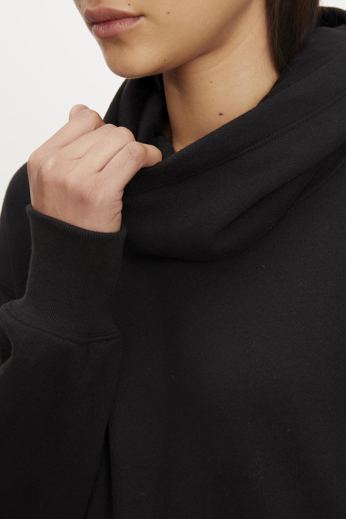   Close-up of a person wearing a black funnel neck YARA SOFT FLEECE HOODIE DRESS with an integrated snood, focusing on the lower half of the face and neck from Velvet by Graham & Spencer. 