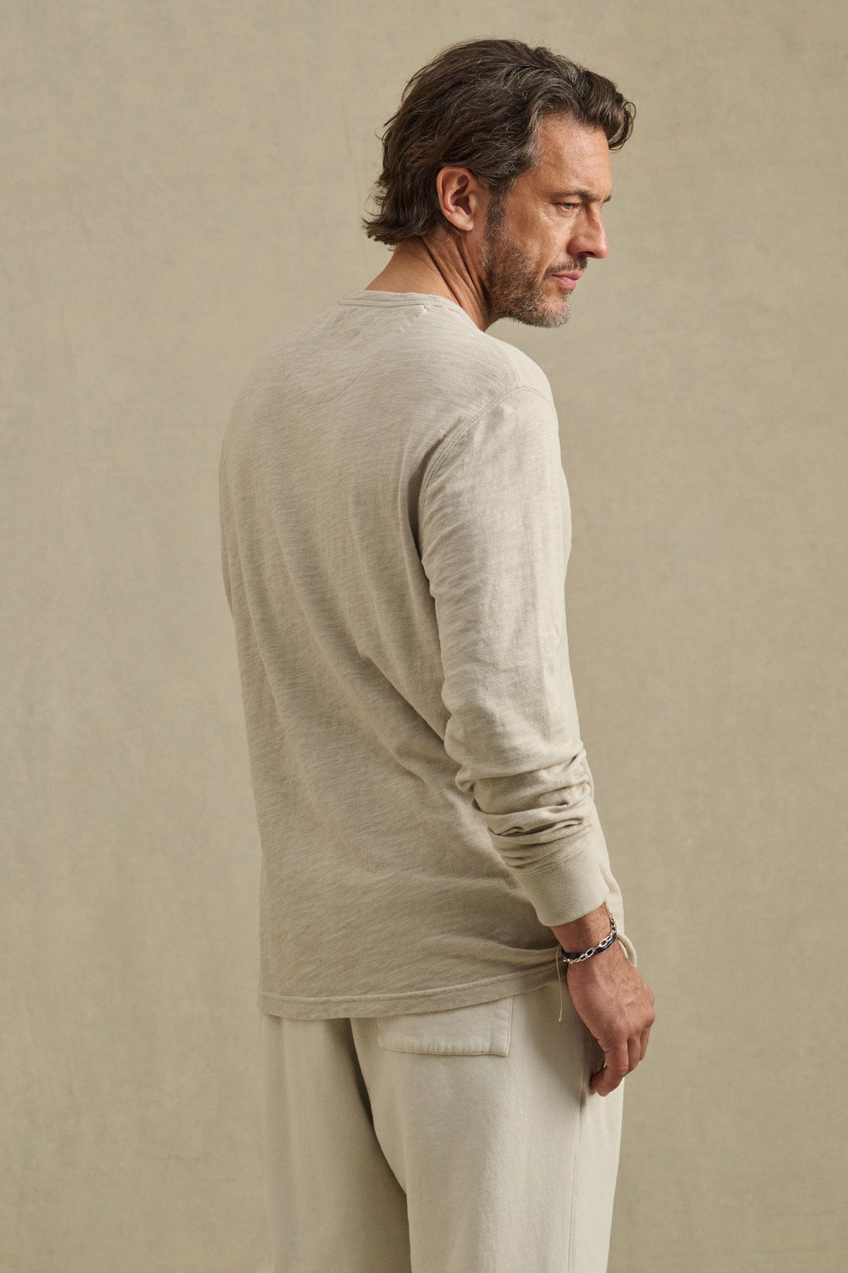 Man with short brown hair and a beard wears the DUSTIN TEE by Velvet by Graham & Spencer with matching pants, standing and looking to the side against a plain background.