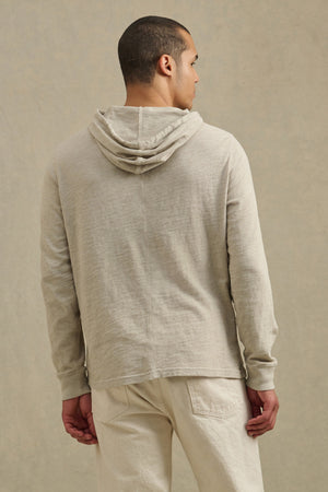 A man faces away from the camera, wearing the FRITZ HOODIE by Velvet by Graham & Spencer in light beige cotton slub, with matching pants, against a plain neutral background.