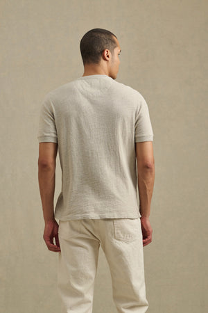 A person faces away, wearing the JENKINS HENLEY by Velvet by Graham & Spencer—a light beige textured shirt styled with matching pants as casual wear against a neutral background.