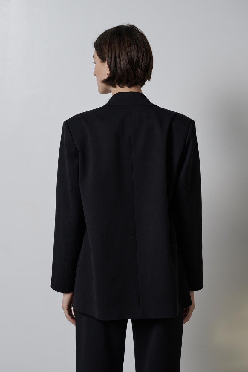 Woman standing with her back to the camera, wearing a black double-breasted Fairfax blazer with a straight-cut silhouette from Velvet by Jenny Graham.