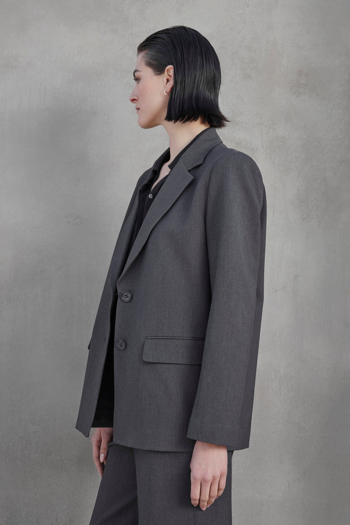   A person with short, dark hair is photographed in profile wearing the REXFORD BLAZER from Velvet by Jenny Graham against a plain, grey background. 