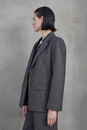 A person with short, dark hair is photographed in profile wearing the REXFORD BLAZER from Velvet by Jenny Graham against a plain, grey background.