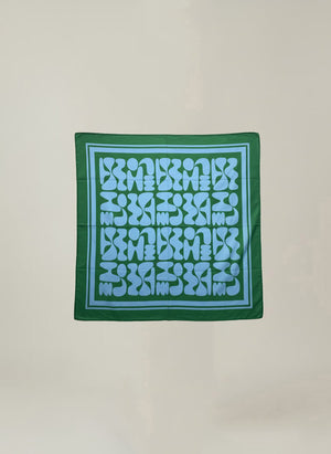 The SOLI SCARF by Velvet by Graham & Spencer is a square green printed cotton scarf with a blue geometric pattern, abstract shapes, and a blue border—a versatile accessory for any wardrobe.