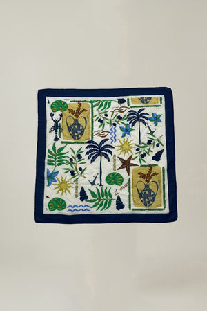 The SOLI SCARF by Velvet by Graham & Spencer features a navy border and embroidered tropical plants, birds, palm trees, and shields in green, blue, brown, and yellow on cream—a versatile accessory for any look.