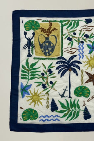 The SOLI SCARF by Velvet by Graham & Spencer is a versatile square accessory with a navy border, embroidered with a vase, palm tree, plants, sun, lobster, anchor, seashells, and the phrase 