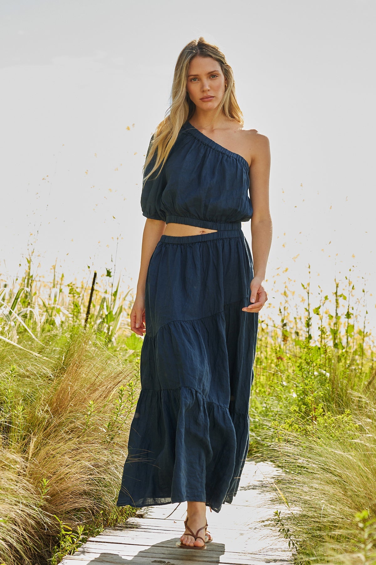 a woman wearing a blue Velvet by Graham & Spencer GISELLE LINEN ONE SHOULDER DRESS and sandals.-26496270532801