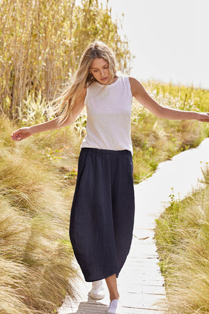A woman is walking down a path with her arms outstretched wearing the Velvet by Graham & Spencer FAE LINEN A-LINE SKIRT.
