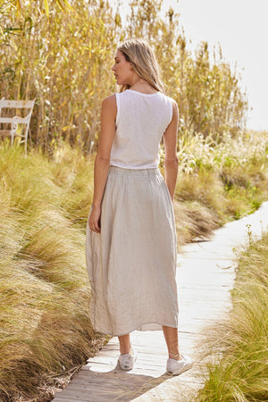 a woman wearing a white t-shirt and a FAE LINEN A-LINE SKIRT by Velvet by Graham & Spencer walking through tall grass.