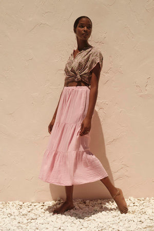 A woman in a pink Danielle Cotton Gauze Tiered Skirt by Velvet by Graham & Spencer with in-seam pockets standing next to a cotton gauze wall.