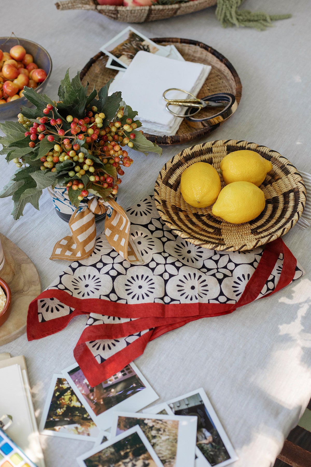 On a table, the NOLA SCARF by Velvet by Graham & Spencer displays lemons in a woven basket, a berry bouquet, and polaroid photos atop lightweight woven cotton. It's a charming scene reminiscent of Cleo Wade's poetic touch.-38895973138625