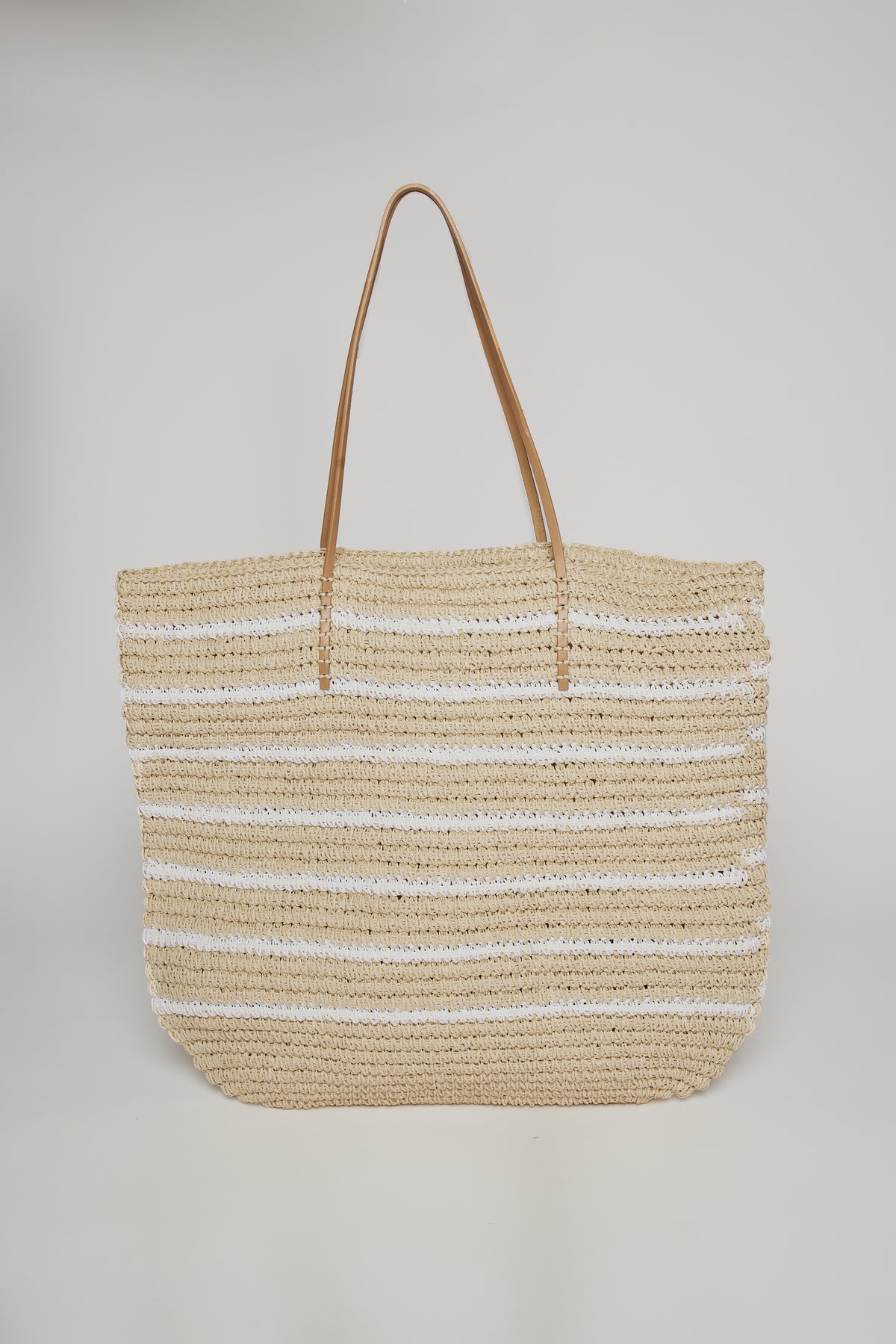   A large STELLA STRIPE TOTE by Velvet by Graham & Spencer, with beige and white stripes, featuring long leather handles, displayed against a plain background. 