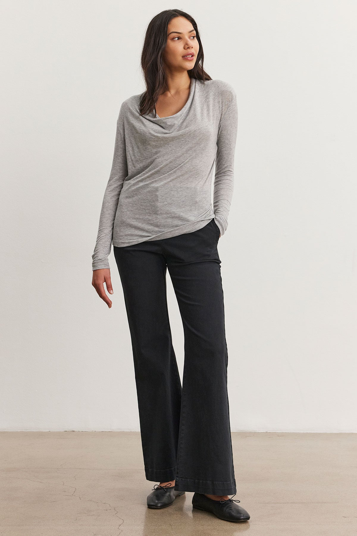   A person wearing the COBIE PANT by Velvet by Graham & Spencer, styled with a gray long-sleeve top and characterized by its polished finish, stands against a plain white background. 