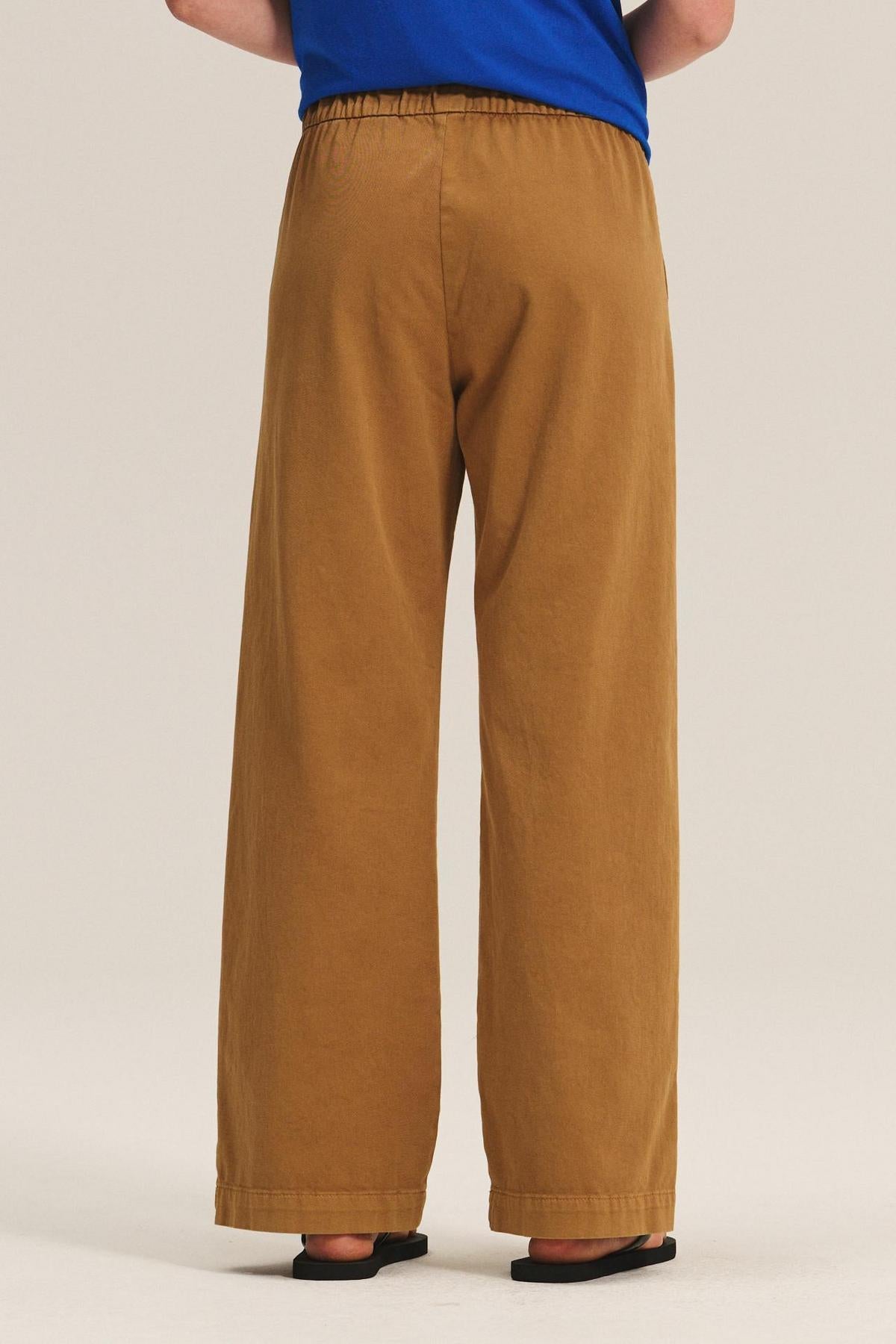 Model shown from the back wearing the NAYA PANT by Velvet by Graham & Spencer—wide-leg style with elastic waistband—paired with a blue top and black sandals against a plain background.