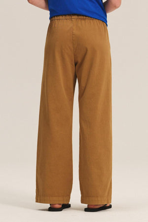 Model shown from the back wearing the NAYA PANT by Velvet by Graham & Spencer—wide-leg style with elastic waistband—paired with a blue top and black sandals against a plain background.