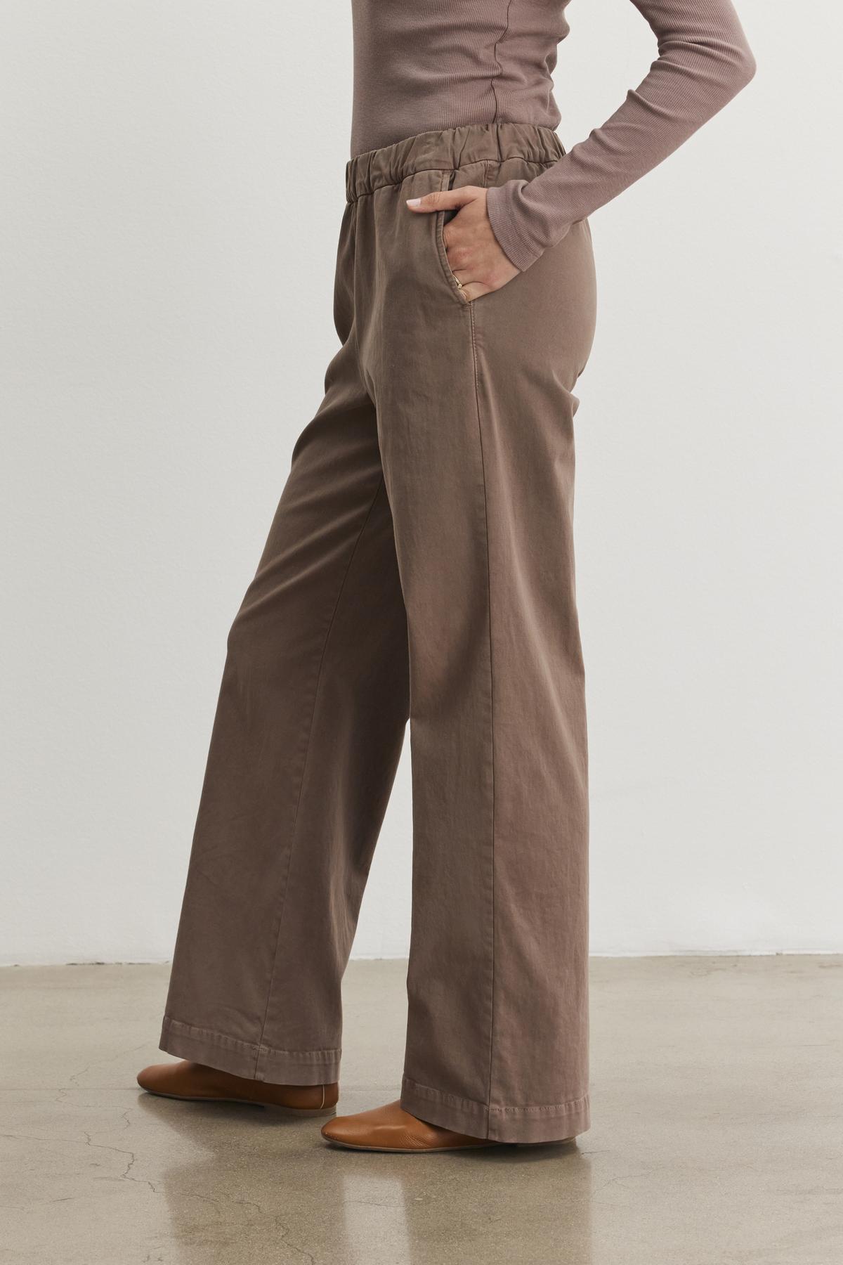   A person wearing the NAYA PANT from Velvet by Graham & Spencer stands gracefully on a polished floor, paired with a long-sleeve top. 