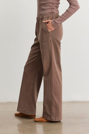 A person wearing the NAYA PANT from Velvet by Graham & Spencer stands gracefully on a polished floor, paired with a long-sleeve top.