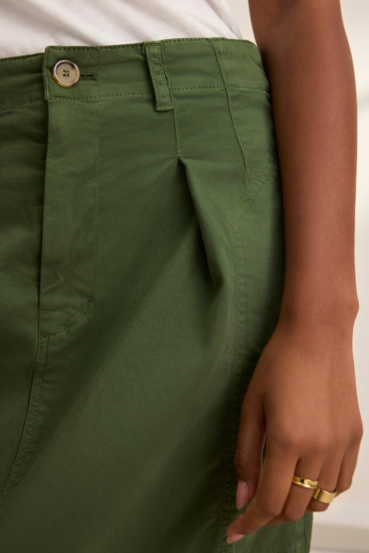Close-up of a person wearing a crisp white shirt, stretch cotton twill green LILIAN SKIRT by Velvet by Graham & Spencer, and a hand adorned with two gold rings.-38662723174593