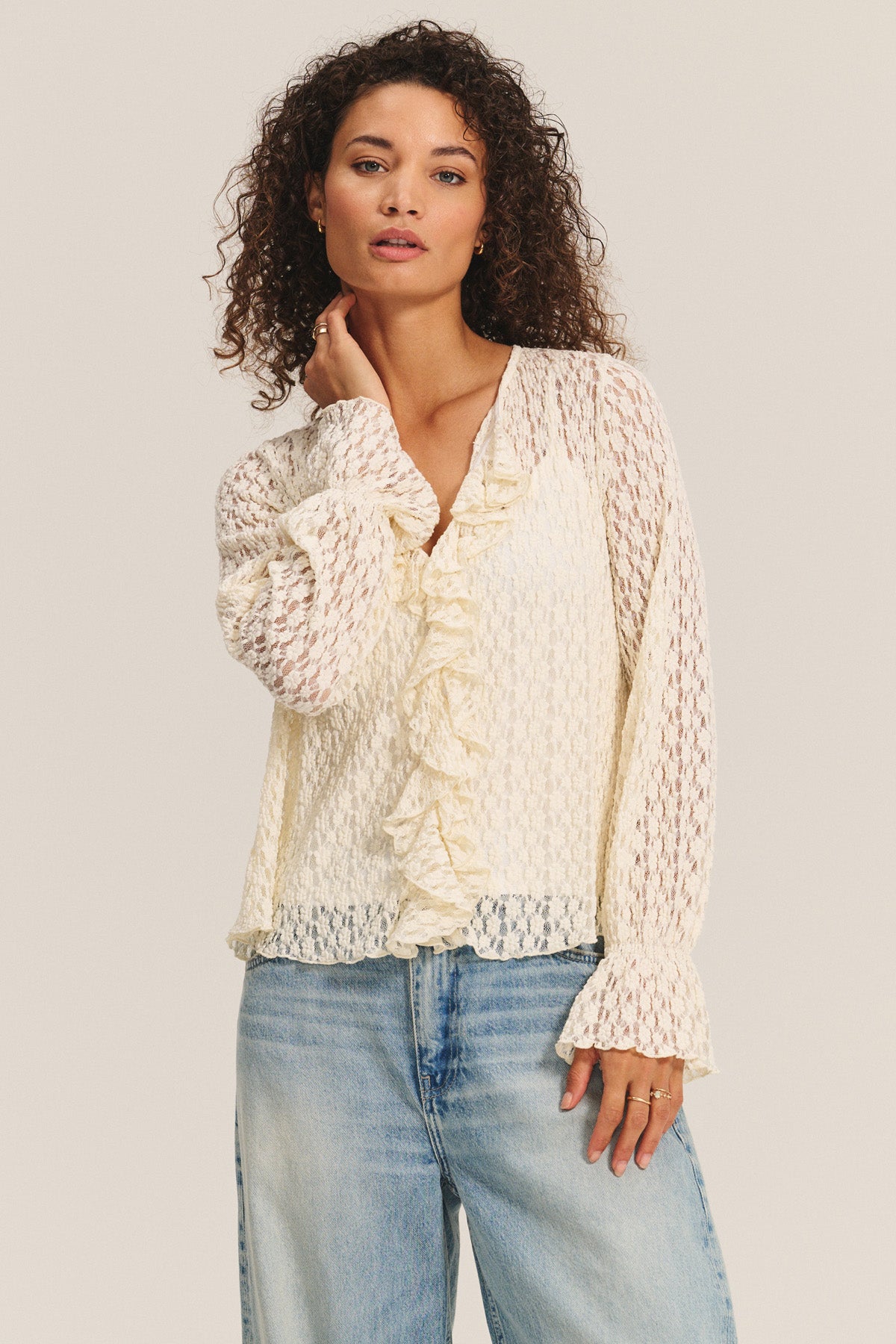 A woman models the NATALIE TOP by Velvet by Graham & Spencer—a cream cotton lace blouse with ruffle details and a detachable cami—paired with light blue jeans, standing against a plain light background.-40263657259201