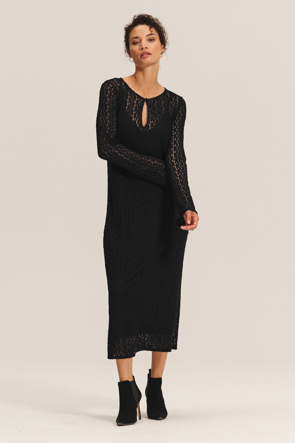 A woman wears the TABITHA DRESS by Velvet by Graham & Spencer, a black long-sleeve knit midi-to-maxi dress with a keyhole neckline, paired with black ankle boots, standing against a plain light background.-40681920856257
