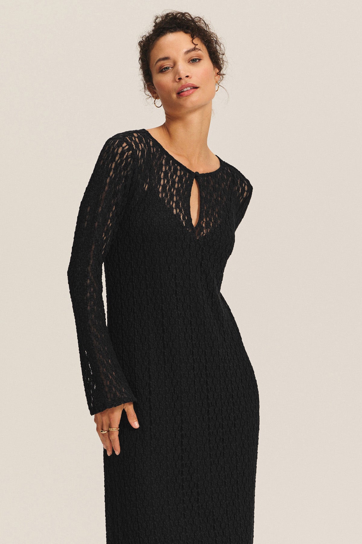 Someone stands against a neutral background wearing the TABITHA DRESS by Velvet by Graham & Spencer—a long-sleeve, black textured midi-to-maxi dress featuring a keyhole neckline.