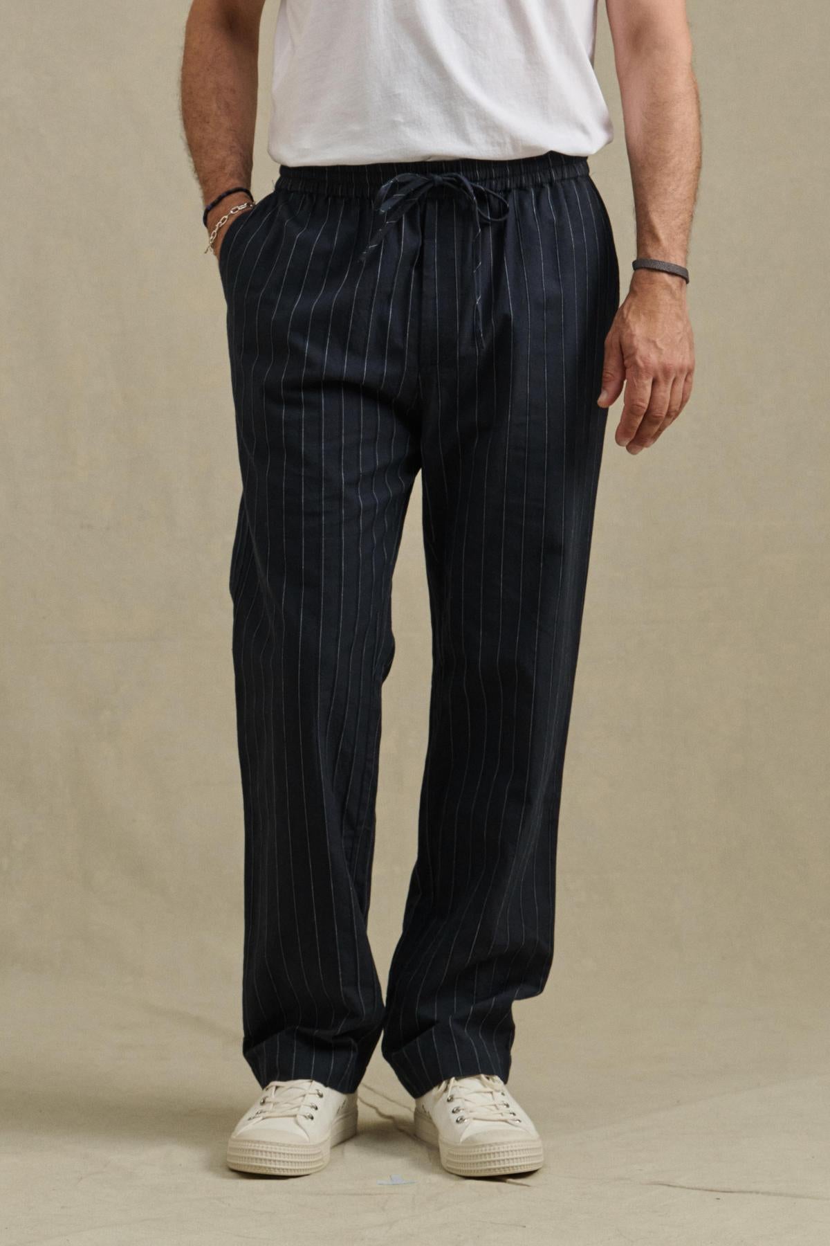A person wearing the SAINT PANT by Velvet by Graham & Spencer, styled with a white t-shirt and white sneakers, stands against a plain background.