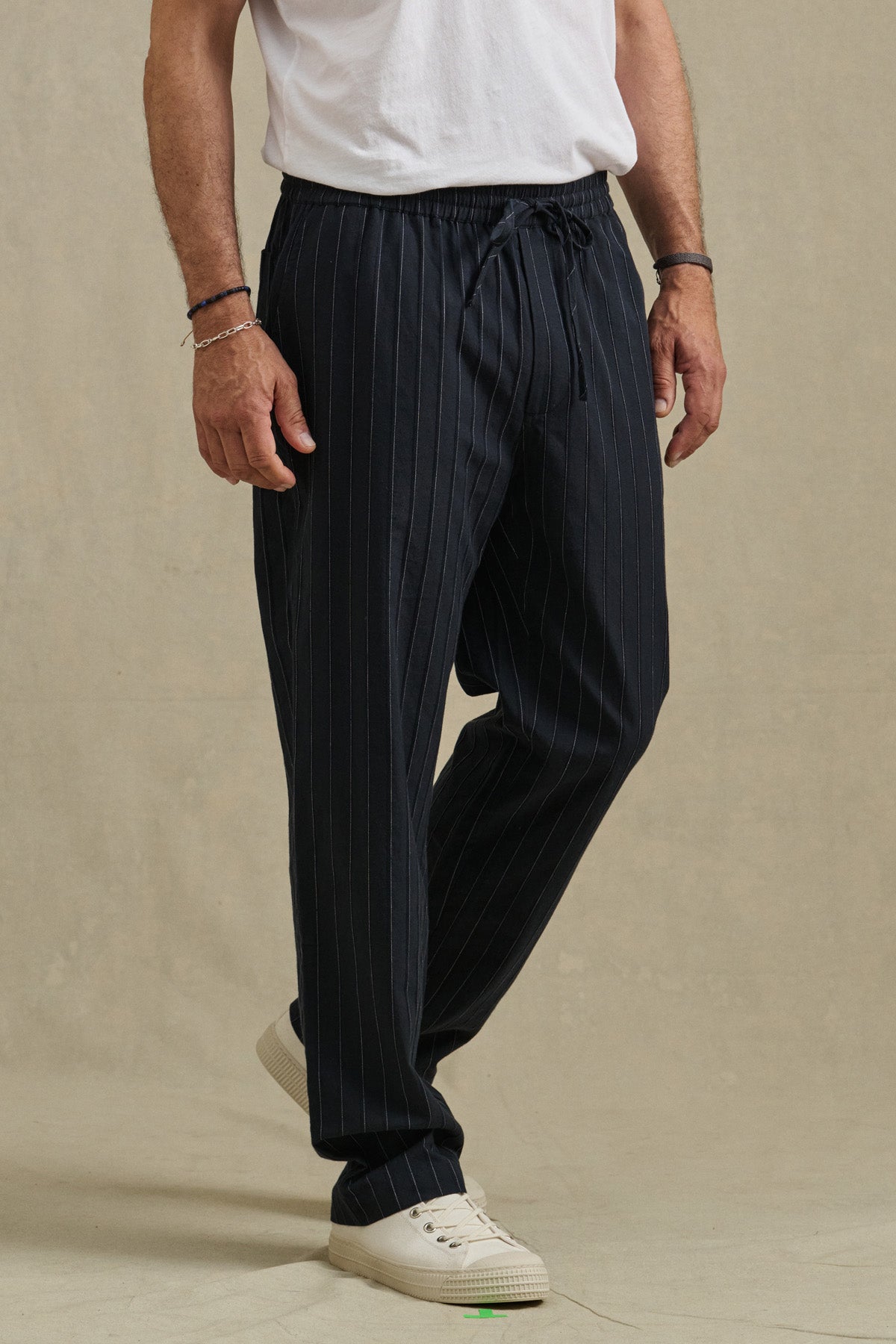 A person wearing Velvet by Graham & Spencer's SAINT PANT stands against a plain beige background, paired with a white t-shirt and white sneakers.-41453974159553