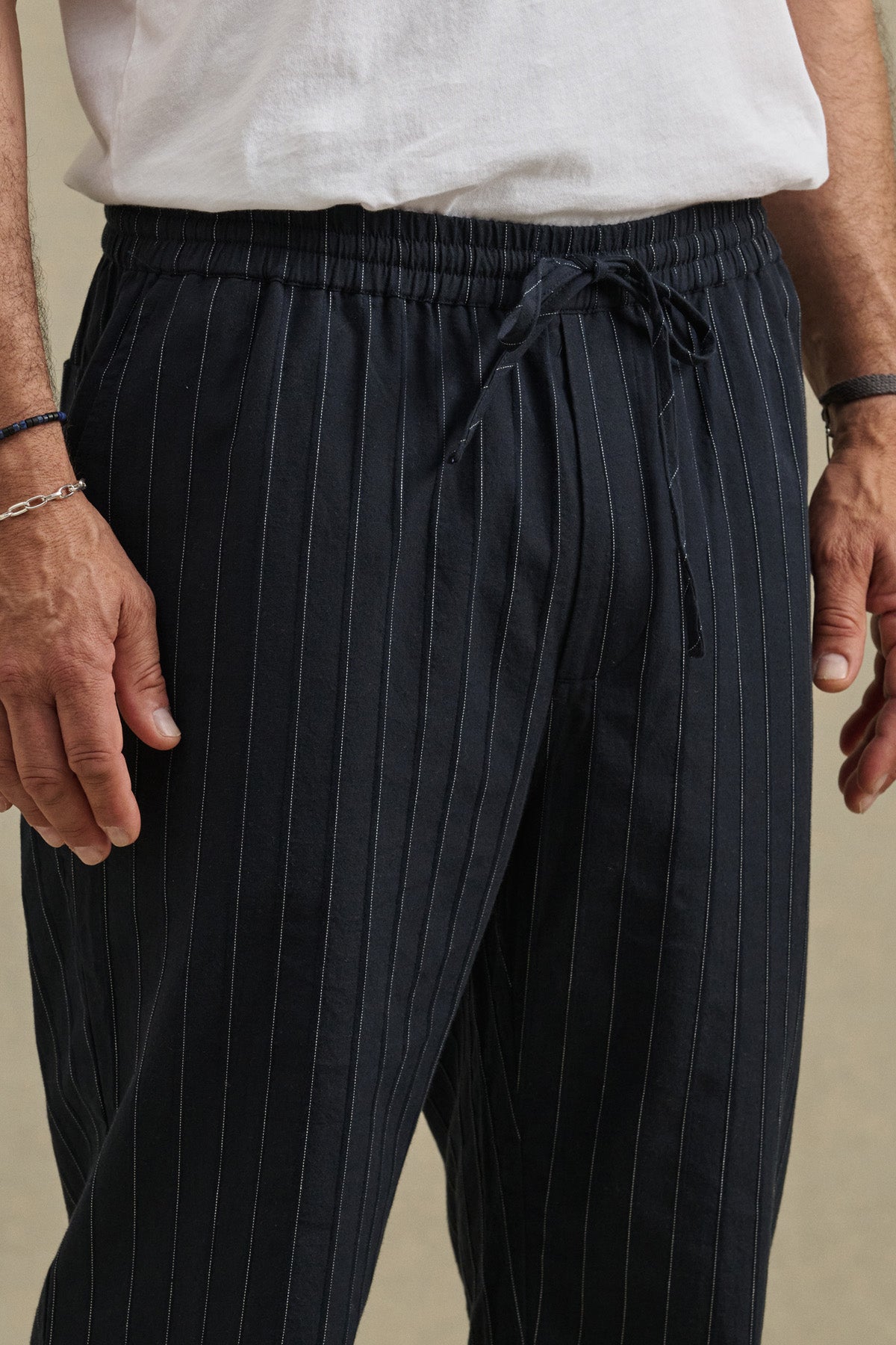 A person wearing a white T-shirt and Velvet by Graham & Spencer SAINT PANT in black pinstripes, hands relaxed at their sides.-41453974225089