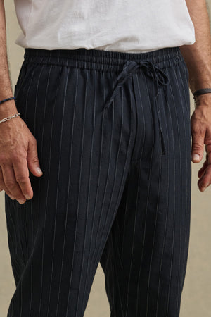 A person wearing a white T-shirt and Velvet by Graham & Spencer SAINT PANT in black pinstripes, hands relaxed at their sides.