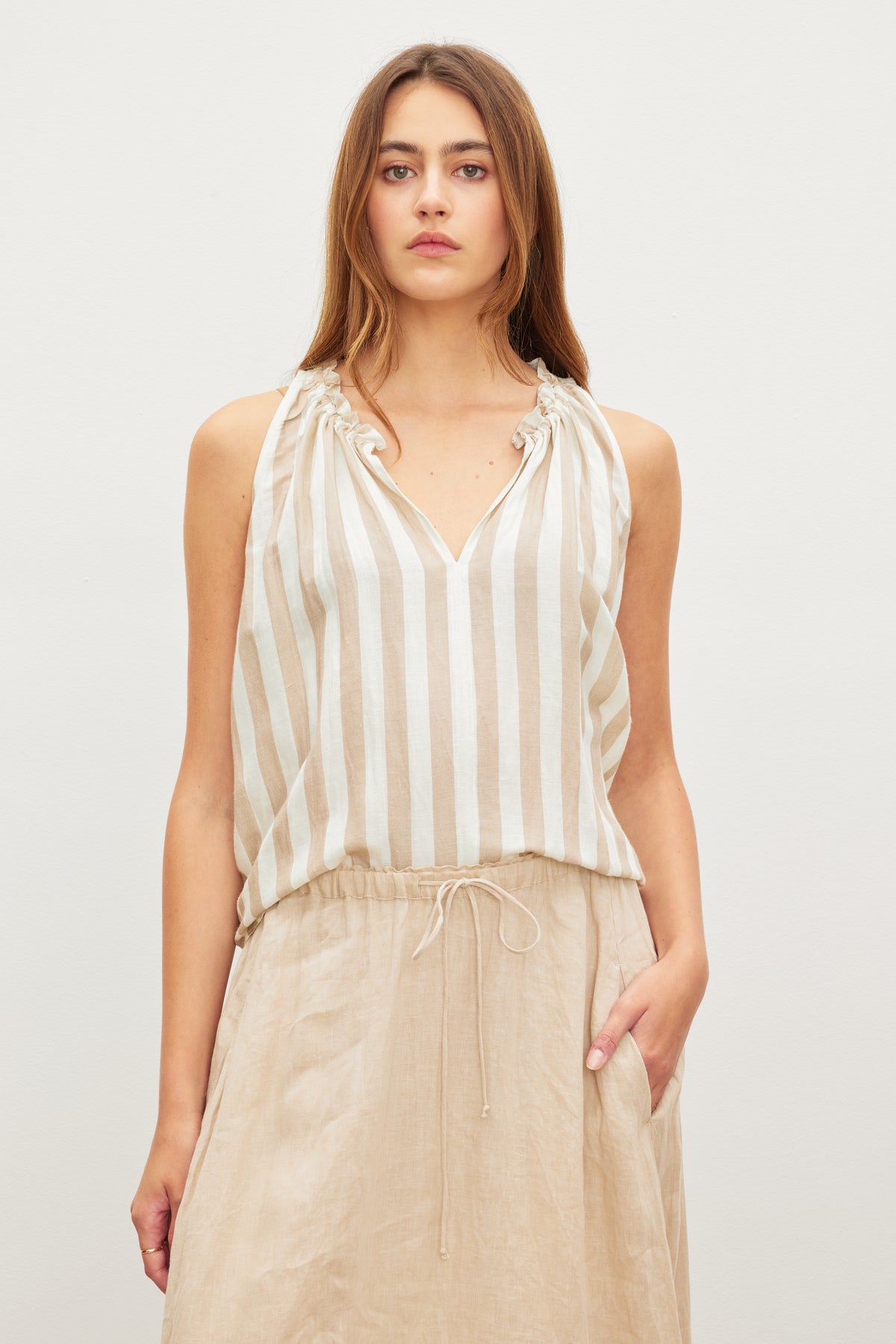 A young woman poses in an ERICA STRIPED LINEN TANK TOP and beige skirt by Velvet by Graham & Spencer.-36580707107009