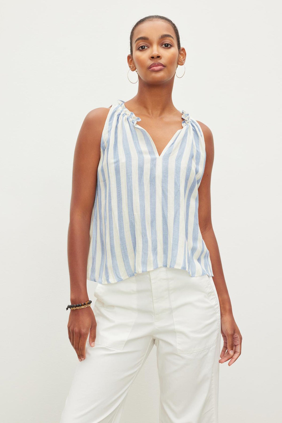   Woman posing in a Velvet by Graham & Spencer ERICA STRIPED LINEN TANK TOP with white pants against a plain background. 