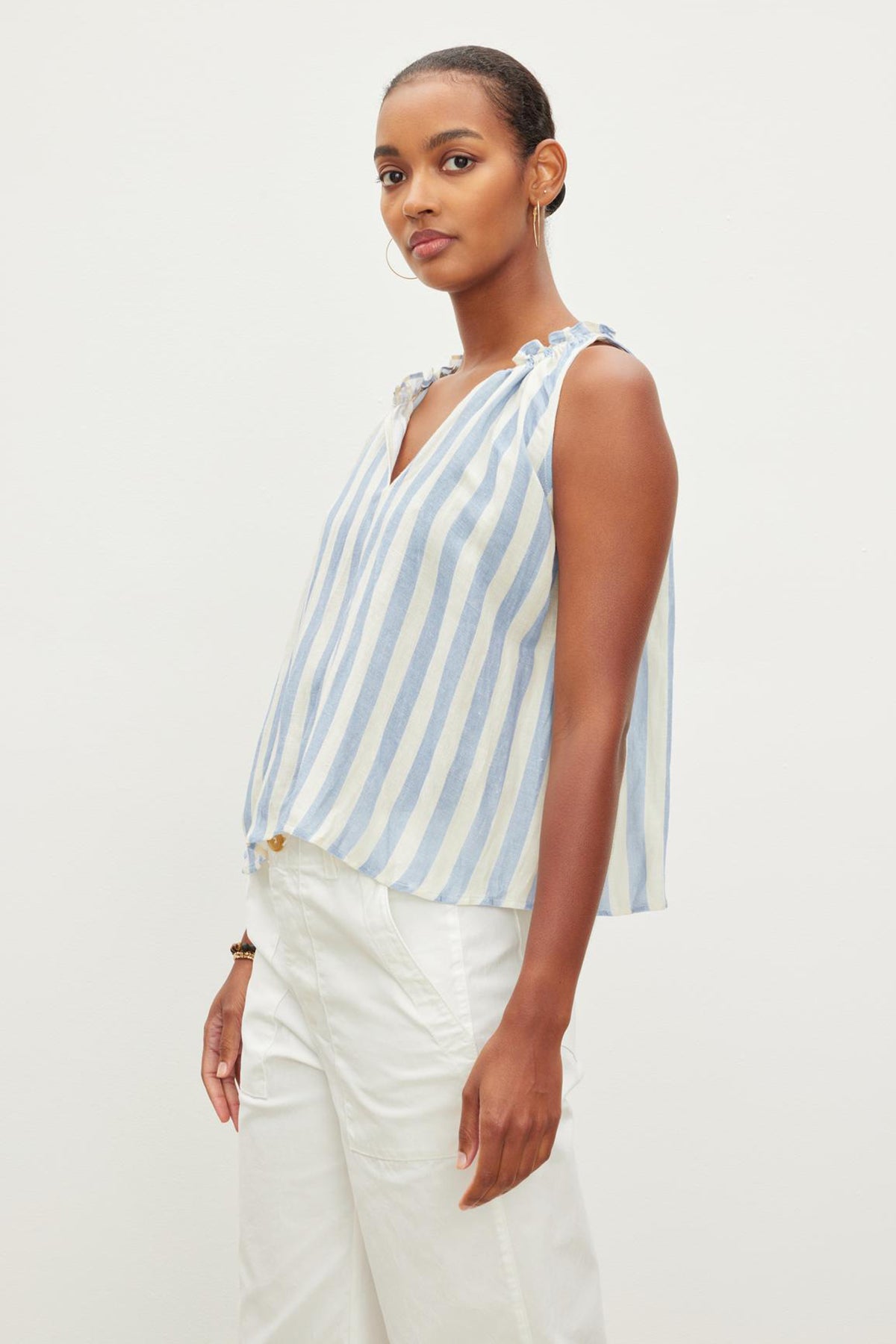   A woman in an ERICA STRIPED LINEN TANK TOP by Velvet by Graham & Spencer and white pants posing against a neutral background. 