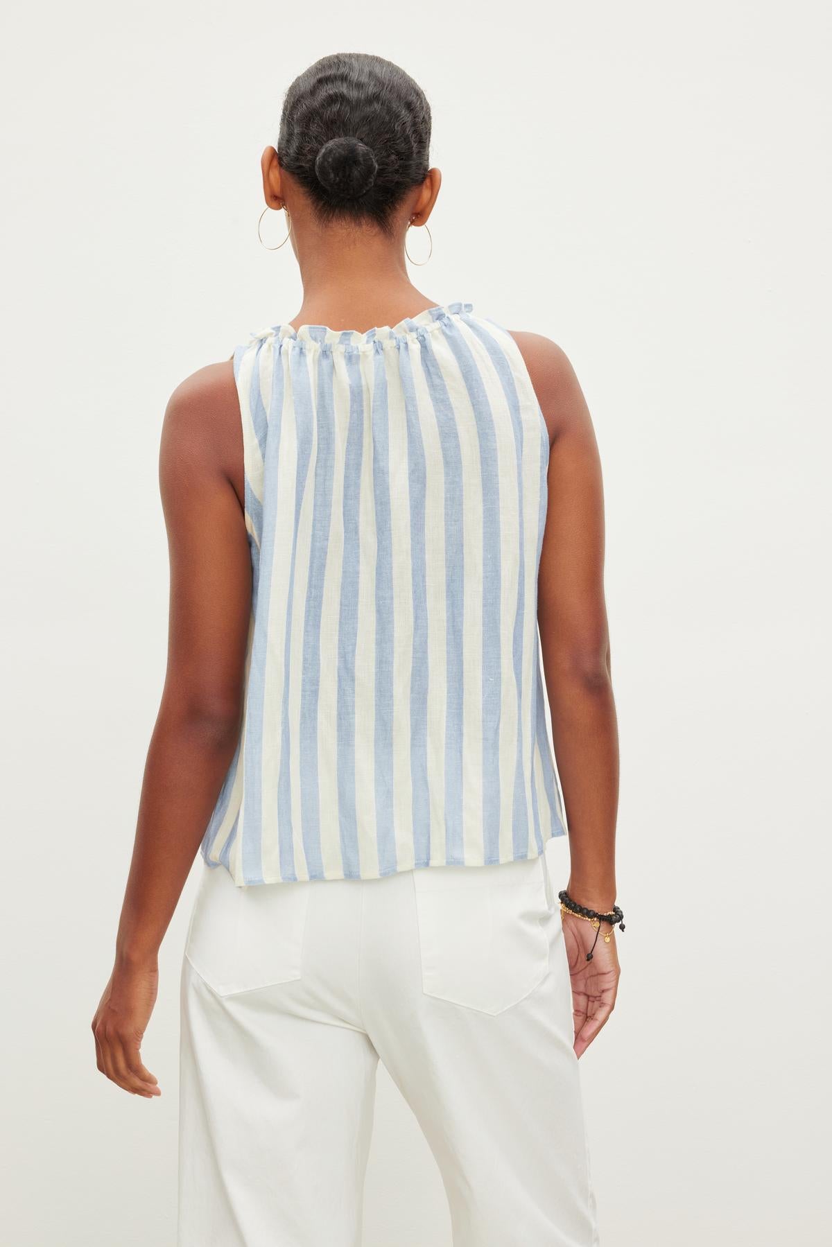   A woman stands with her back to the camera, wearing a sleeveless ERICA STRIPED LINEN TANK TOP by Velvet by Graham & Spencer and white pants. 