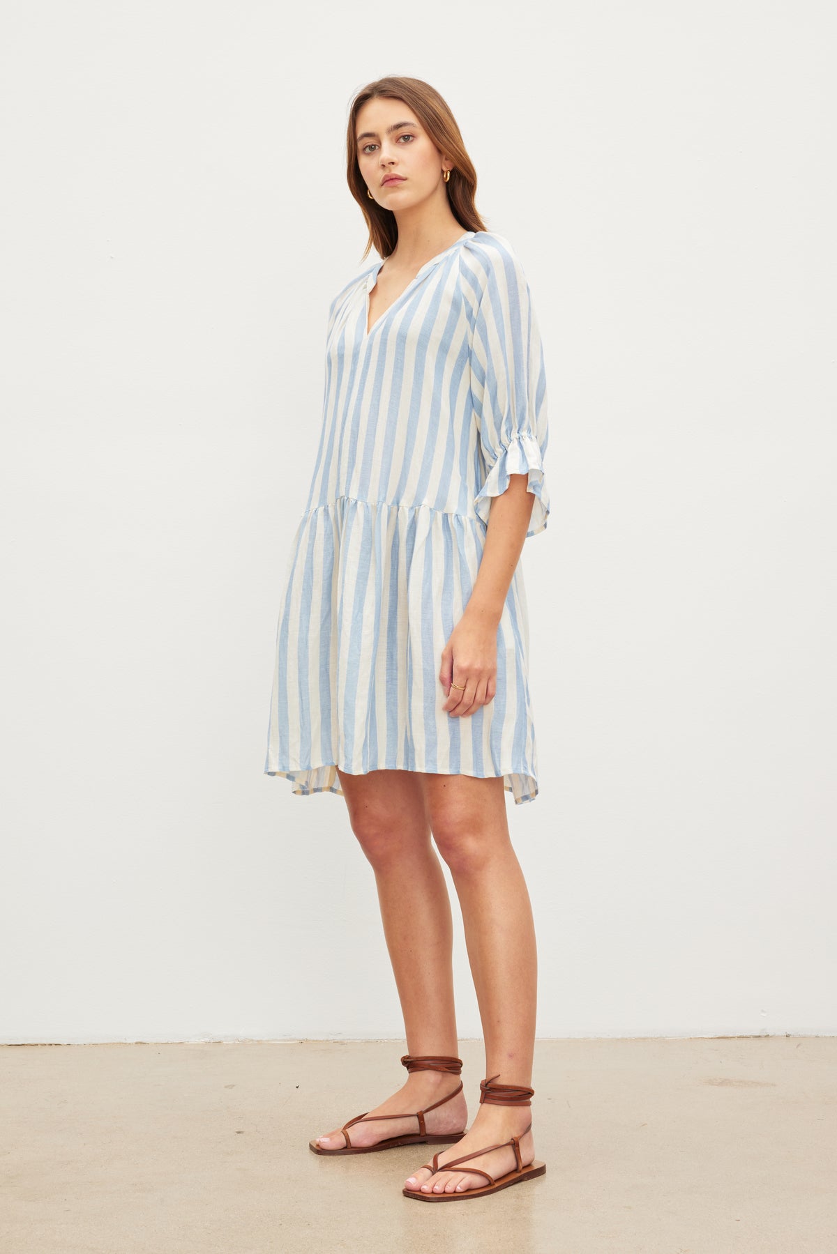   A woman posing in a Velvet by Graham & Spencer JESSICA STRIPED LINEN DRESS and flat sandals against a plain background. 