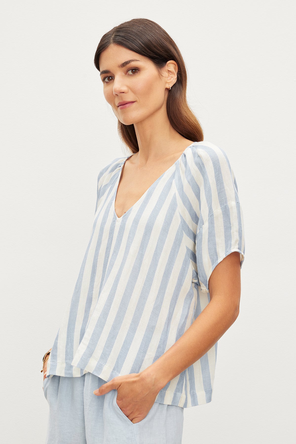   The model is wearing a relaxed fit blue and white striped top, the KATY STRIPED LINEN TOP, with West Coast vibes from Velvet by Graham & Spencer. 