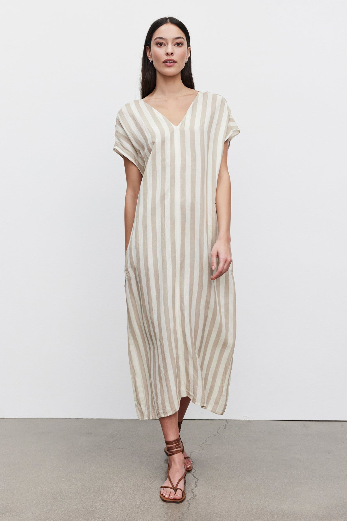 A woman in a MILLA STRIPED LINEN KAFTAN DRESS by Velvet by Graham & Spencer and brown strappy sandals stands against a plain background.-36247892558017