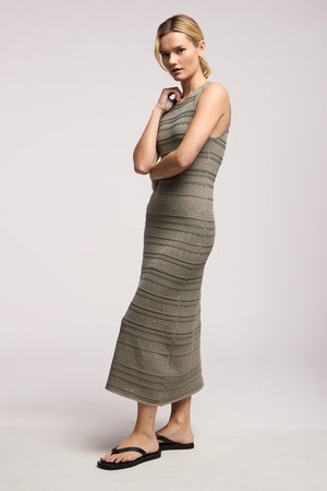 A woman wears the YLENA DRESS by Velvet by Graham & Spencer, a sleeveless, textured olive stripe pointelle midi with an A-line hem, paired with black sandals against a plain light background.