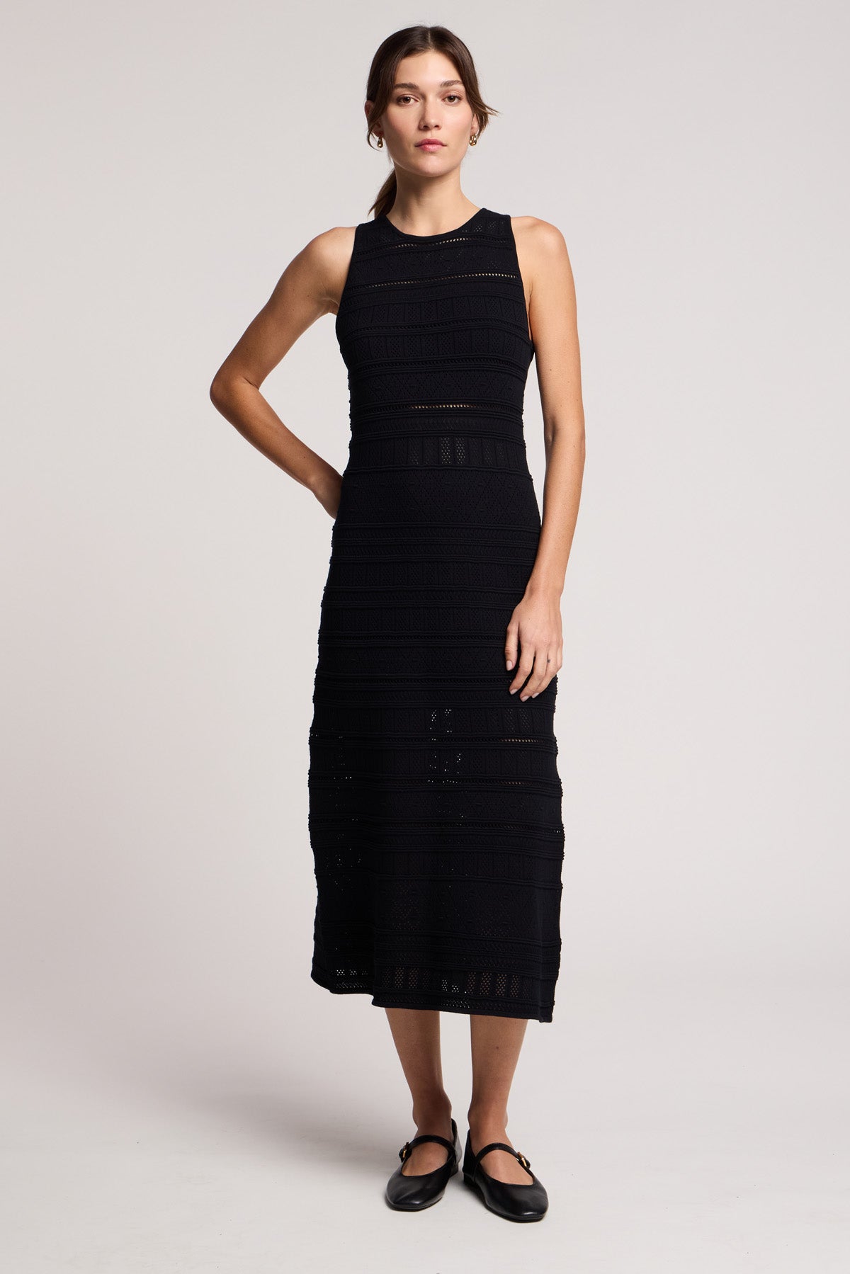 A woman stands against a plain background wearing the YLENA DRESS by Velvet by Graham & Spencer, a sleeveless textured midi with a fitted A-line silhouette, paired with black Mary Jane shoes for an elegant look.