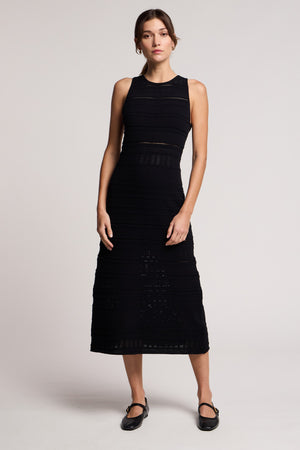 A woman wears the YLENA DRESS by Velvet by Graham & Spencer, a sleeveless textured midi in a fitted A-line silhouette, paired with black Mary Jane shoes against a plain light background.