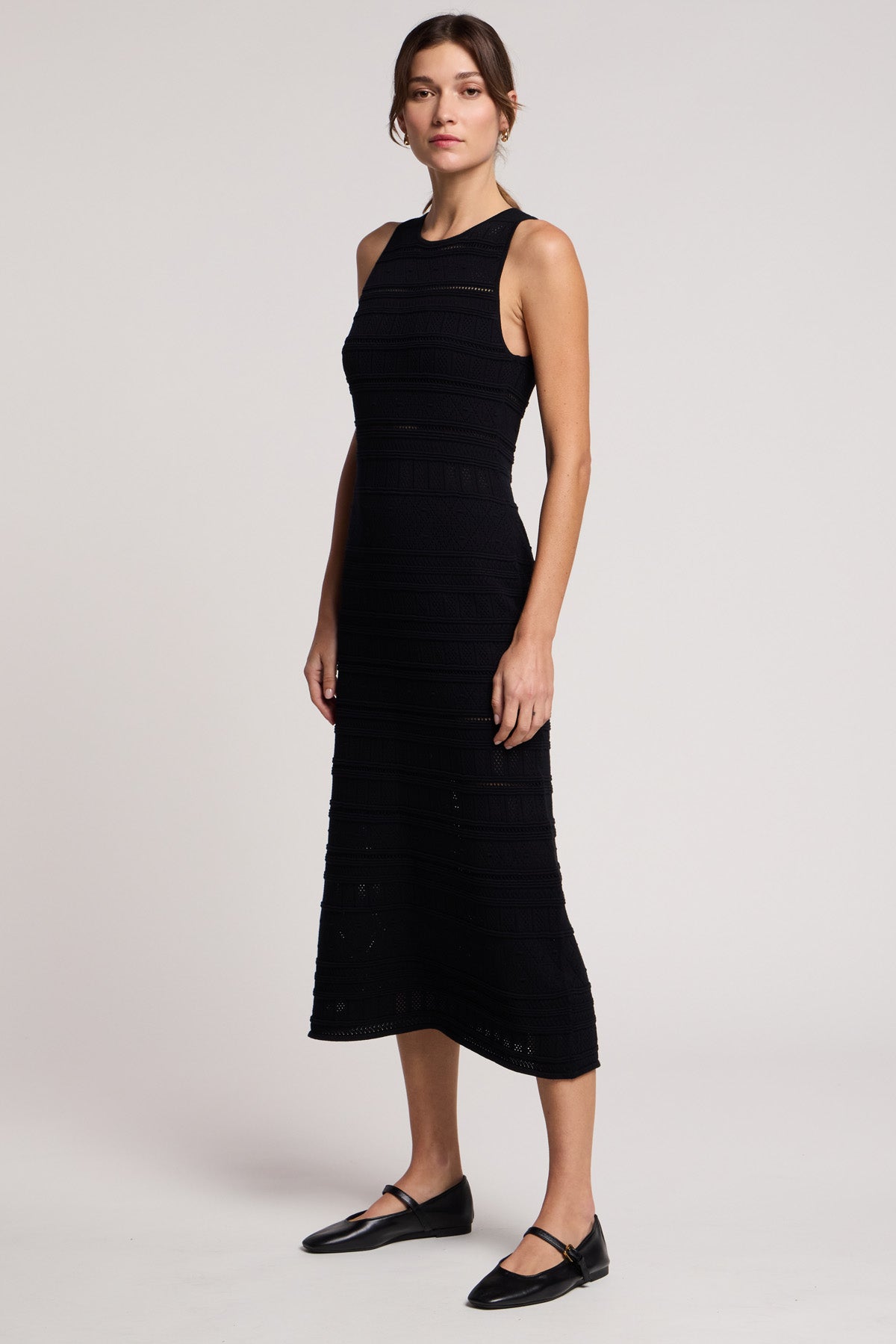 A woman stands against a plain light background wearing the YLENA DRESS by Velvet by Graham & Spencer, a sleeveless midi dress with a fitted waist, paired with black flat shoes.-41645207814337