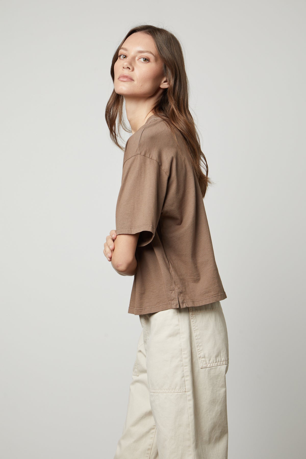 The model is wearing a brown CLARAH CREW NECK TEE by Velvet by Graham & Spencer and white pants, showcasing the sueded jersey fabric.-35655921139905