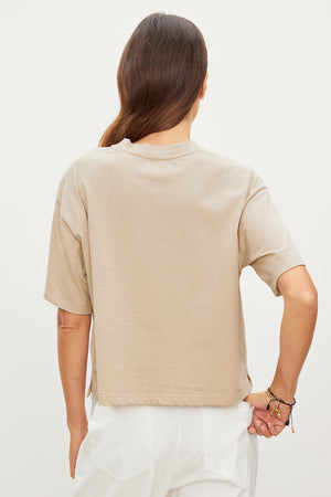 The relaxed back view of a woman wearing a beige CLARAH CREW NECK TEE by Velvet by Graham & Spencer featuring sueded jersey fabric.