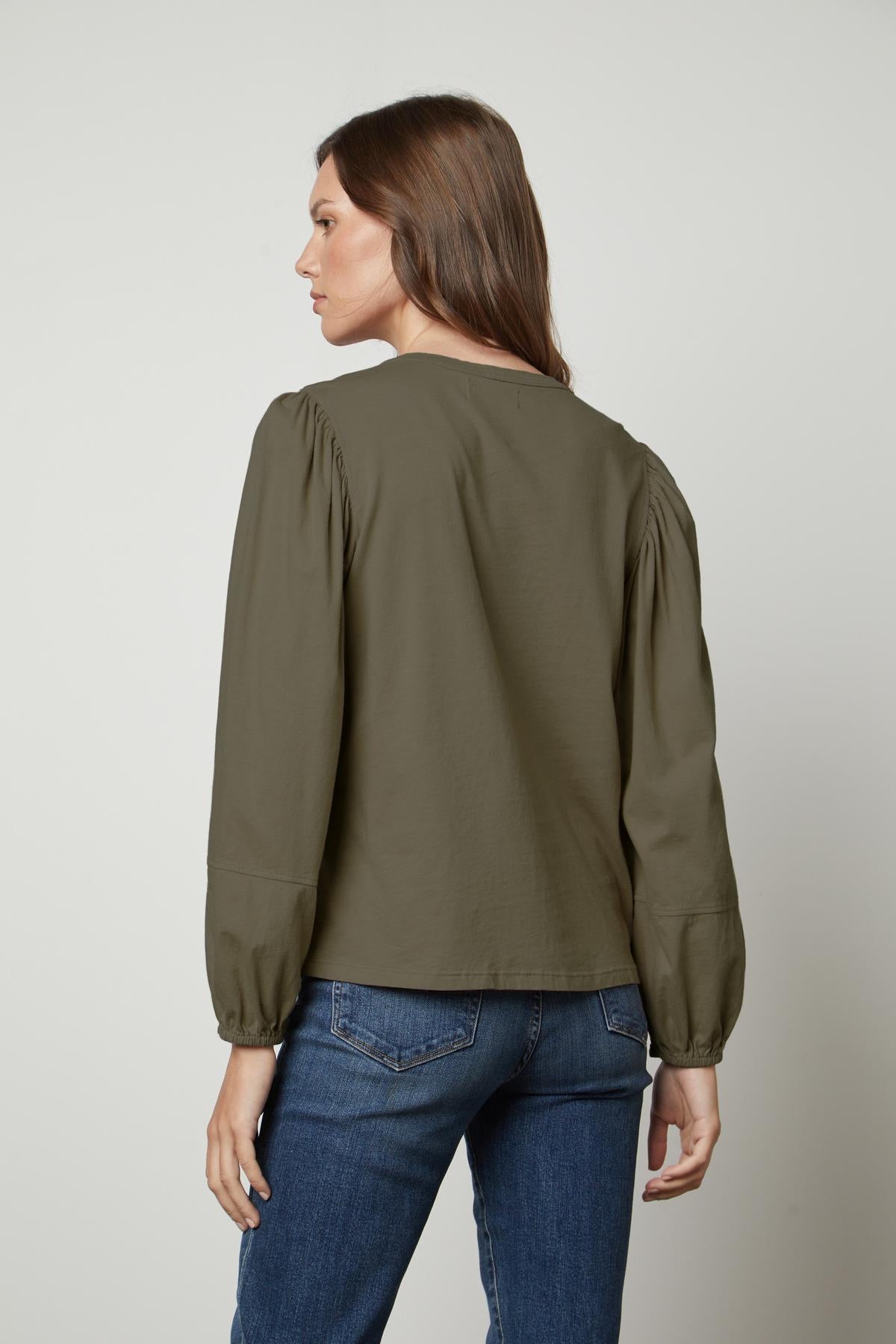 The back view of a woman wearing jeans and a green blouse with a JETTY CREW NECK TEE by Velvet by Graham & Spencer.-35660271616193