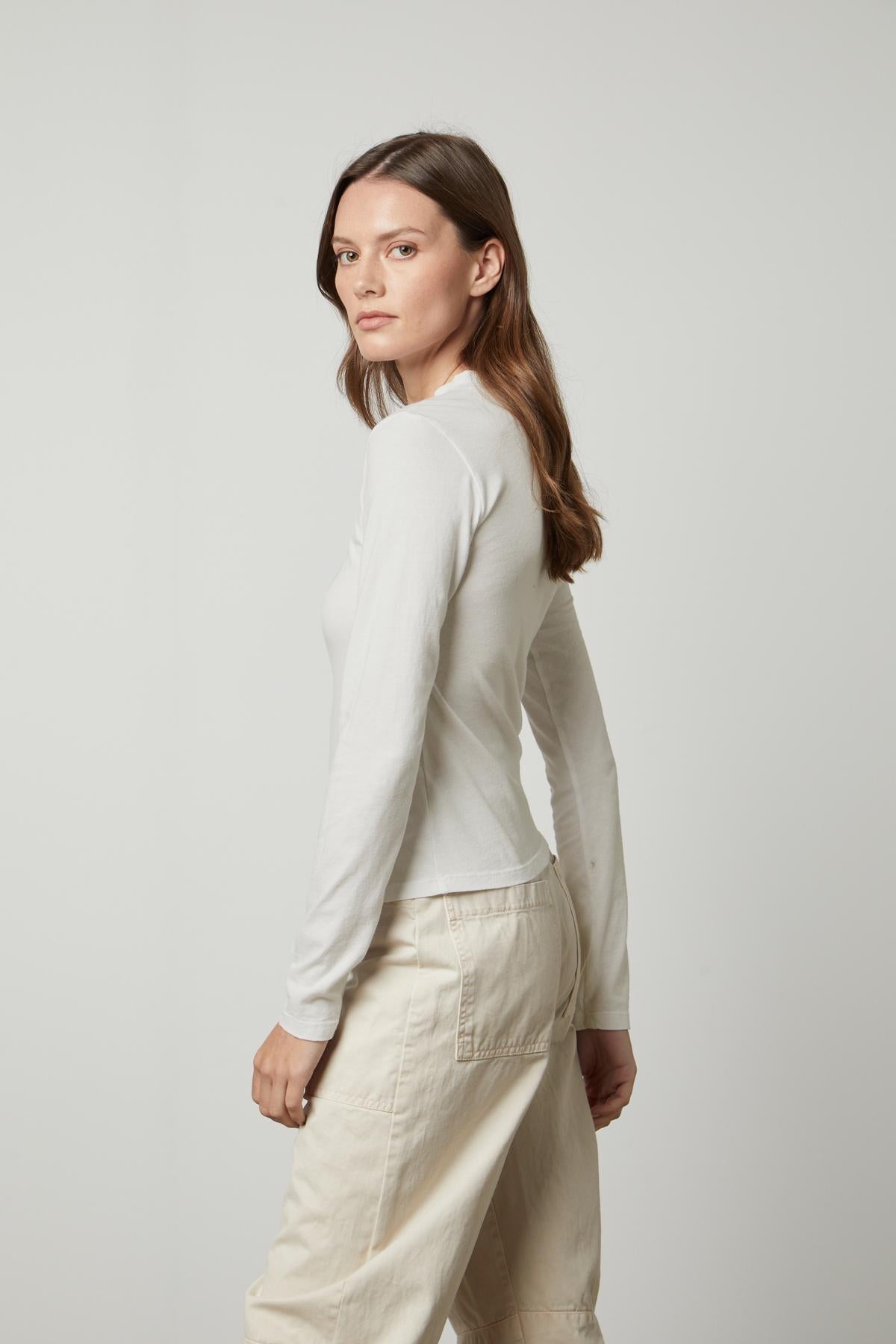 The silhouette is wearing a white Linny Mock Neck Tee top by Velvet by Graham & Spencer and beige trousers, providing a perfect fit.-35660506726593