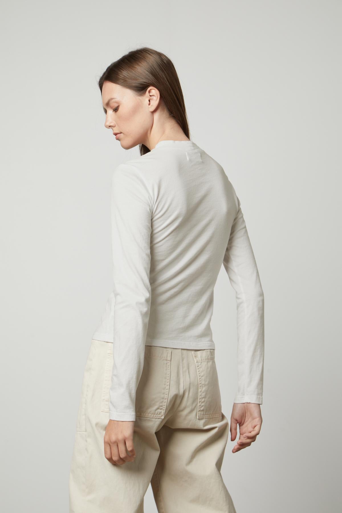   The silhouette of a woman wearing a Velvet by Graham & Spencer LINNY MOCK NECK TEE and beige pants. 