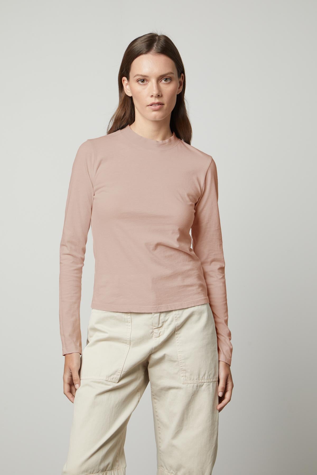 The model is wearing a LINNY MOCK NECK TEE made by Velvet by Graham & Spencer, a pink fitted long-sleeved t-shirt made of sueded jersey.-35660506759361