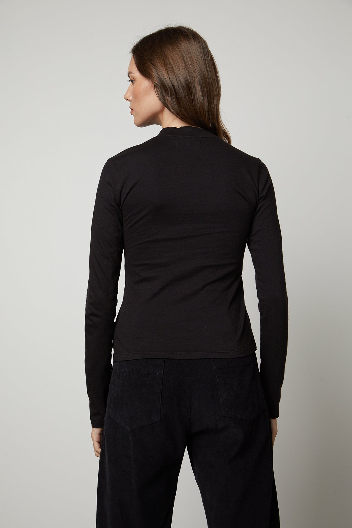   The back view of a woman wearing a Velvet by Graham & Spencer LINNY MOCK NECK TEE fitted silhouette and a long-sleeved top. 
