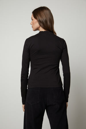 The back view of a woman wearing a Velvet by Graham & Spencer LINNY MOCK NECK TEE fitted silhouette and a long-sleeved top.