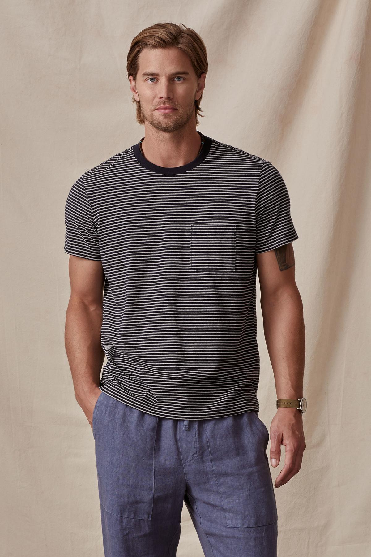 A man in a CHAZZ TEE from Velvet by Graham & Spencer stands against a beige backdrop, looking directly at the camera with a slight smile.-36732512993473